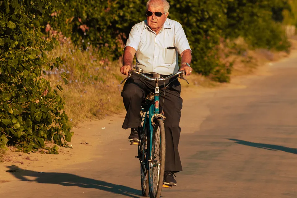 Een oudere man fietst over een landweg in de zon