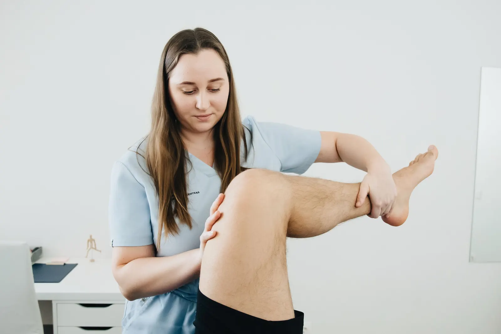Een fysiotherapeut onderzoekt de knie van iemand op de behandeltafel, in daglicht