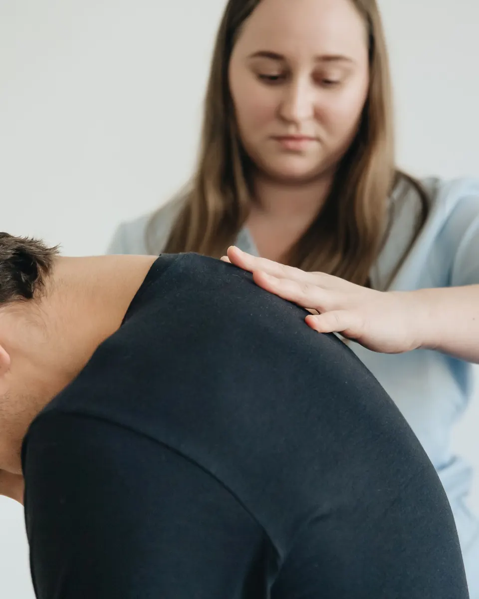 Een fysiotherapeut legt haar hand op de schouder van een man die voorover buigt