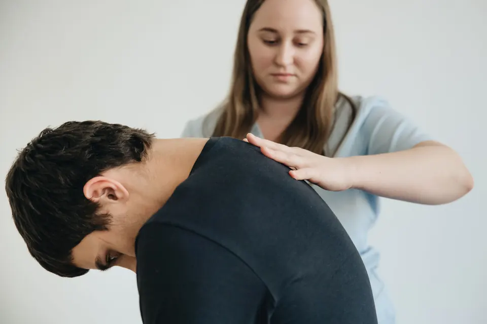 Een fysiotherapeut legt haar hand op de schouder van een man die voorover buigt