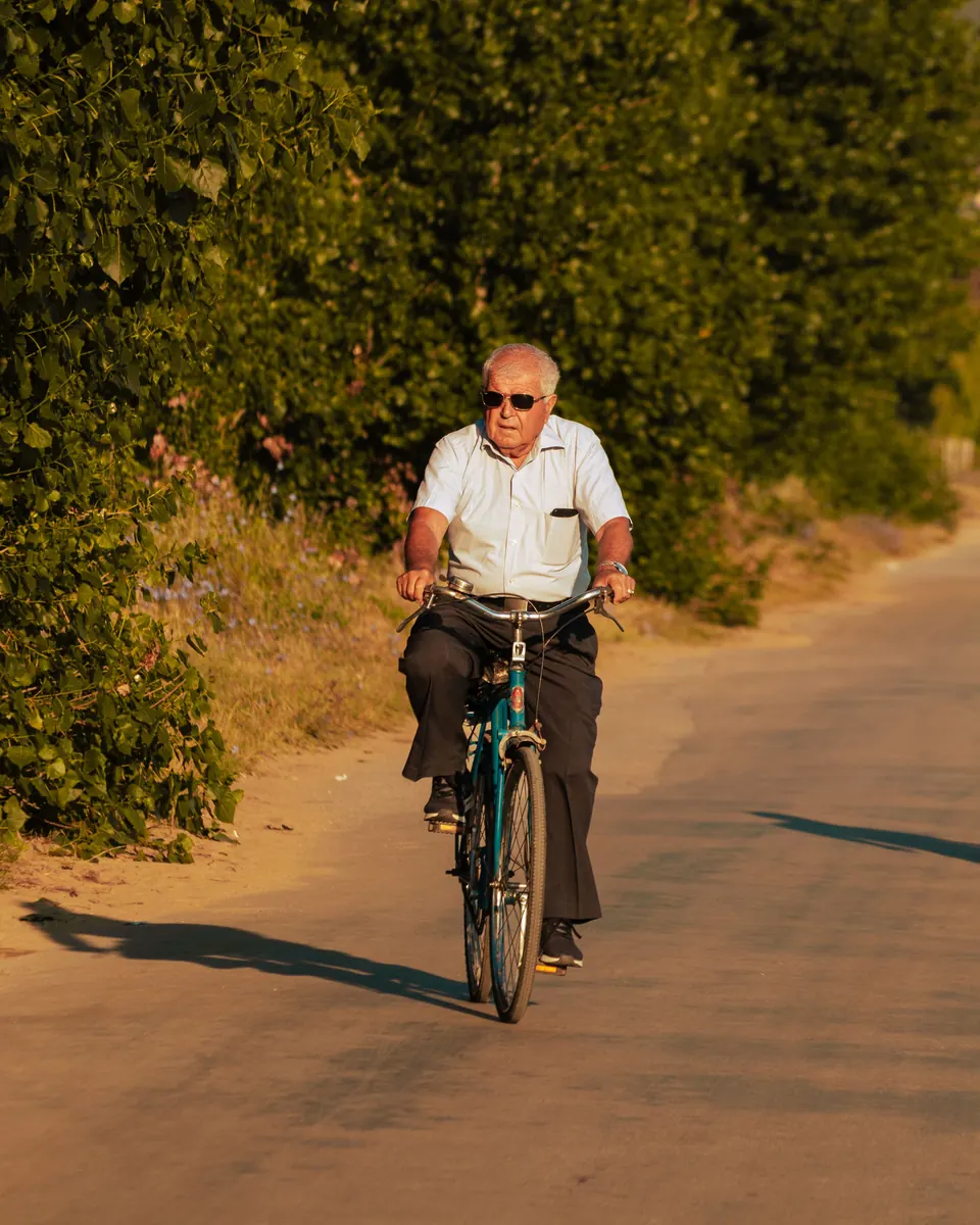Een oudere man fietst over een landweg in de zon